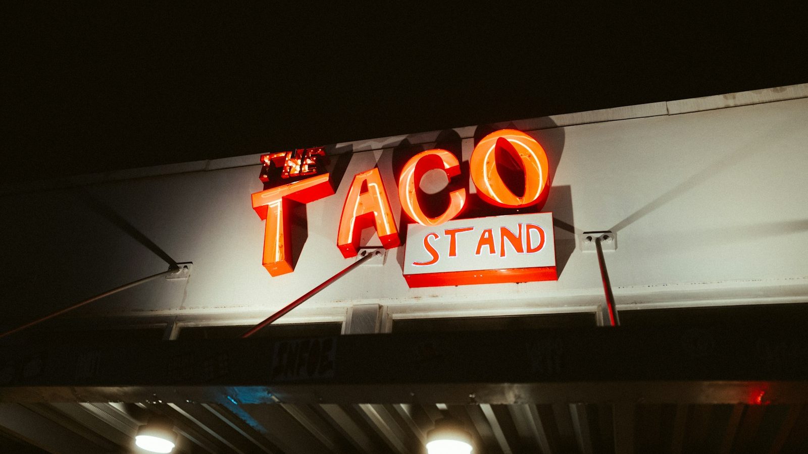 밤에 켜진 「TACO STAND」 네온 간판이 처마 아래에서 붉게 빛나고 있다